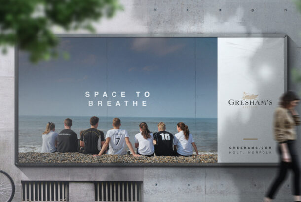 Billboard showing Gresham's School advert with students sat on the beach looking out to sea.