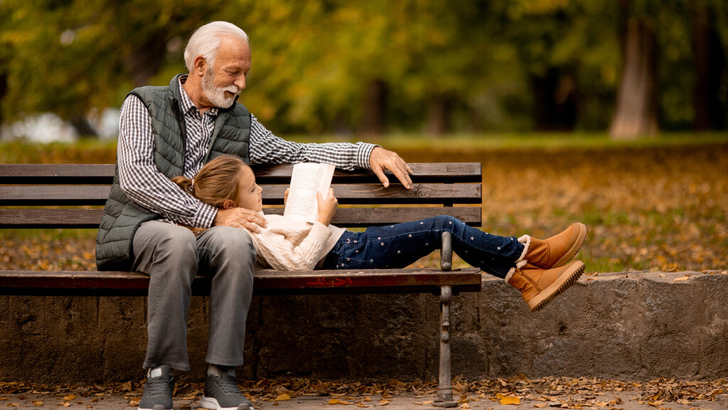 Young girl with her head on her Grandad's lap, sitting on a bench in a park.