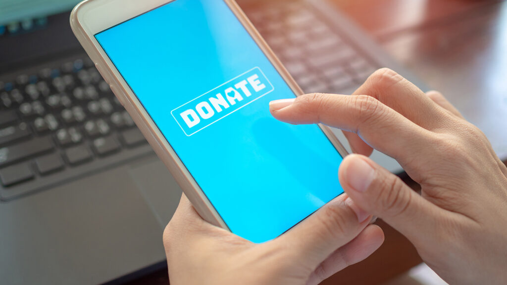 Finger pointing to a donate button on a mobile phone.